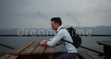 孤独的人在山里。 年轻的帅哥把头靠在手臂上，坐在桌子旁，视野很好